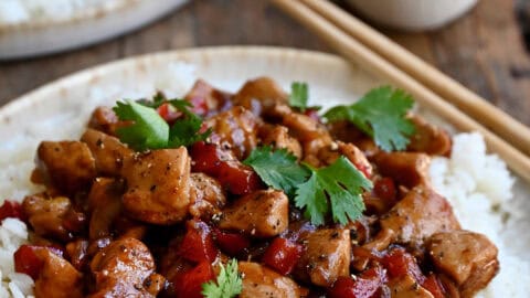 Black pepper chicken over white rice on a plate with chopsticks.