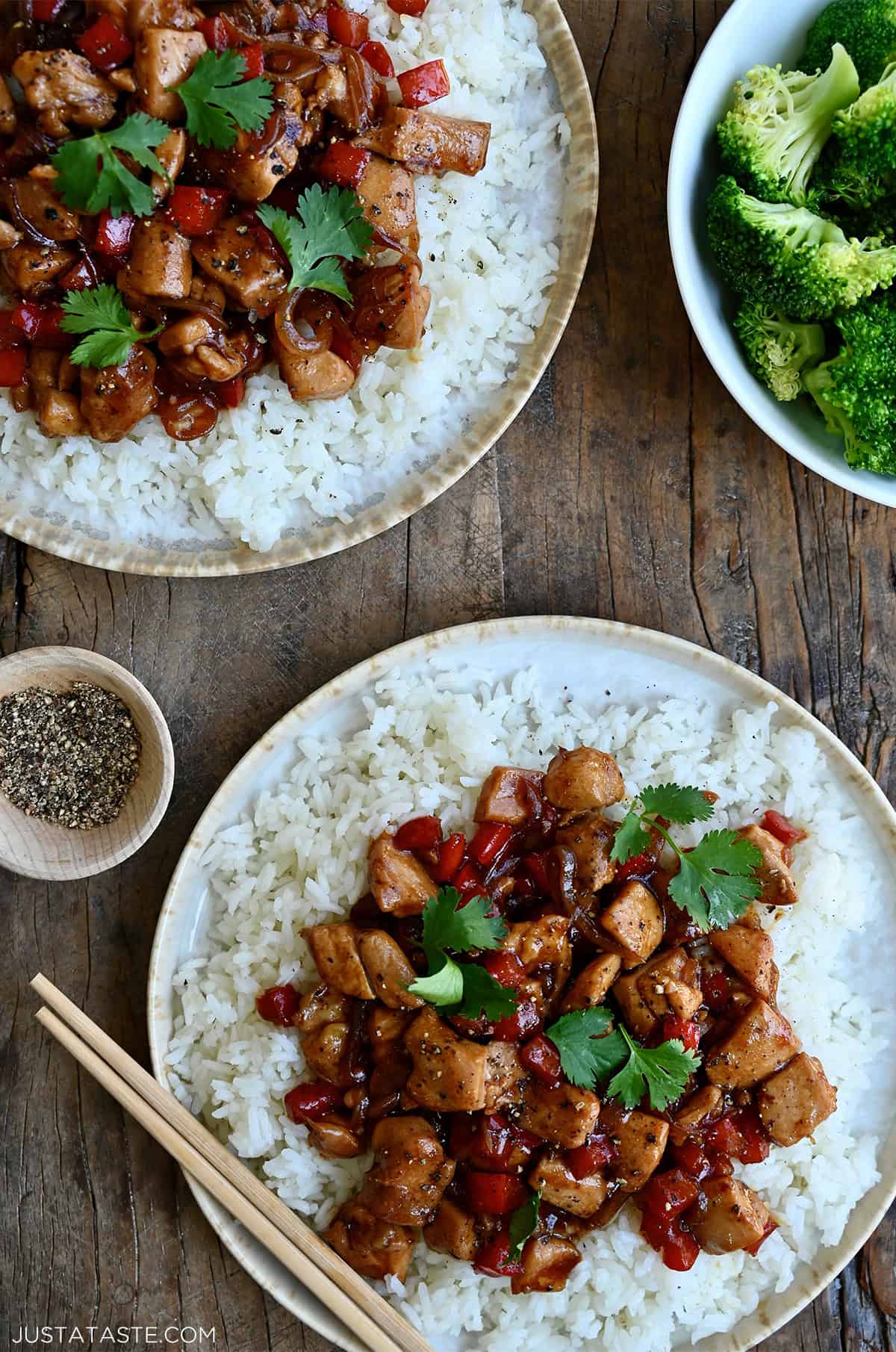 Two dinner plates with steamed white rice topped with black pepper chicken.