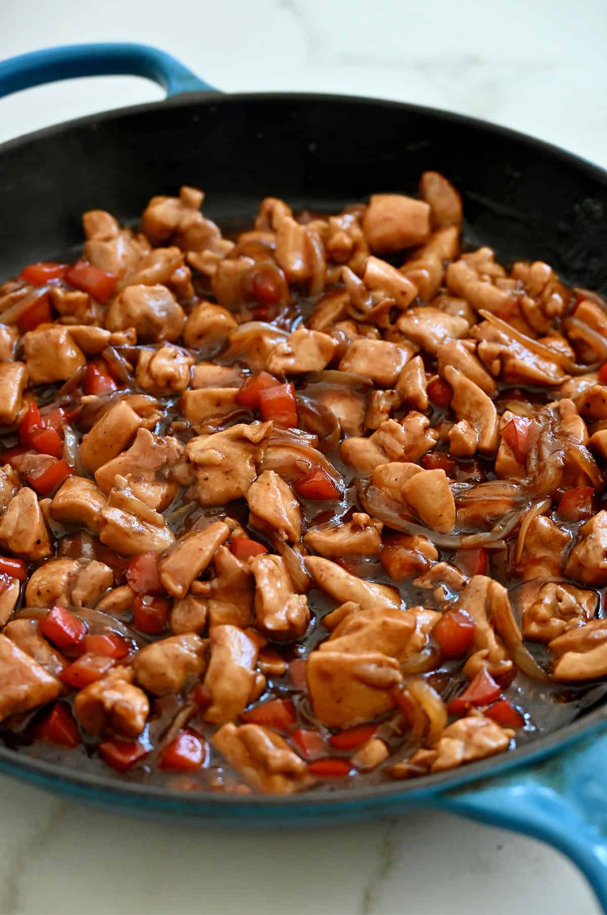 A skillet containing stir-fried chicken with onions and red bell pepper in a black pepper sauce.