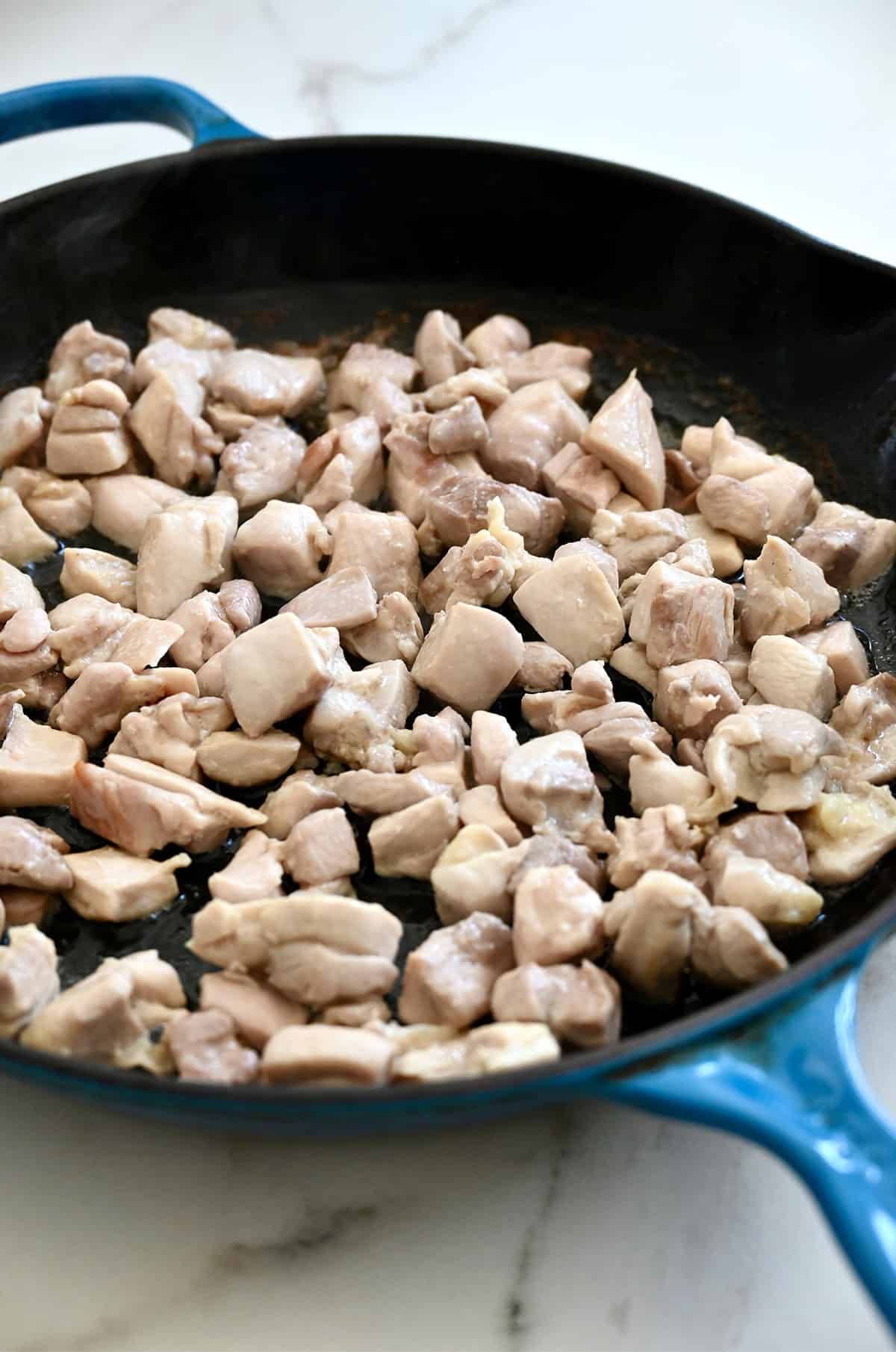Chicken thigh pieces cooking in a skillet.