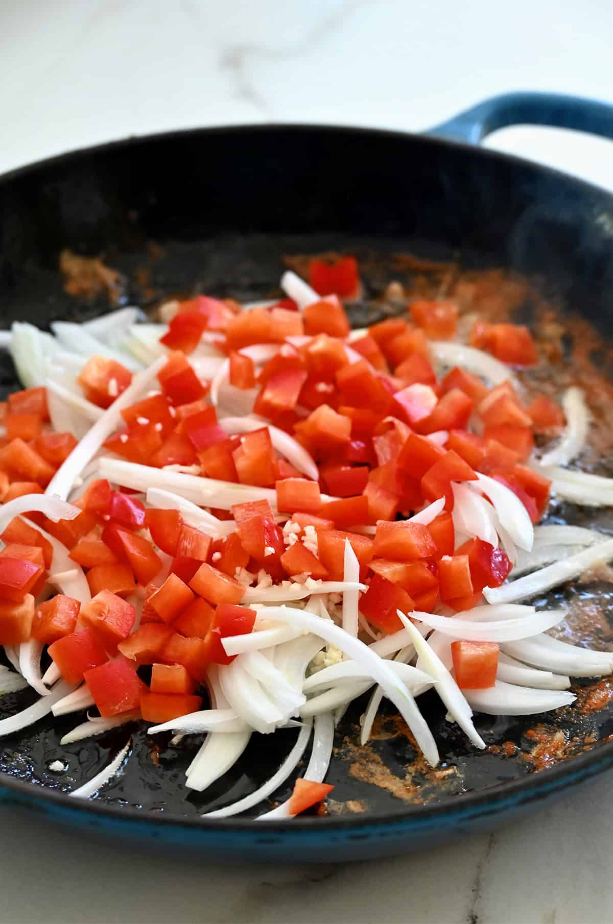 Chopped red bell pepper and sliced onions in a skillet.