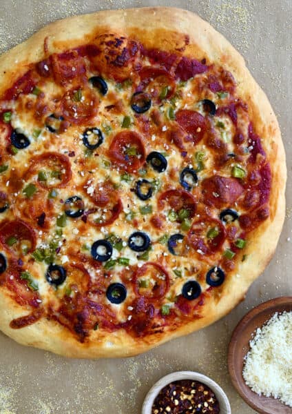 A homemade pizza dough topped with pizza sauce, pepperoni, black olives, green peppers and mozzarella cheese.
