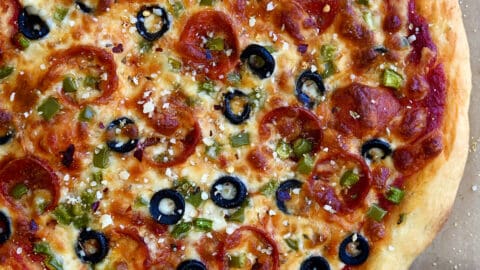 A homemade pizza dough topped with pizza sauce, pepperoni, black olives, green peppers and mozzarella cheese.