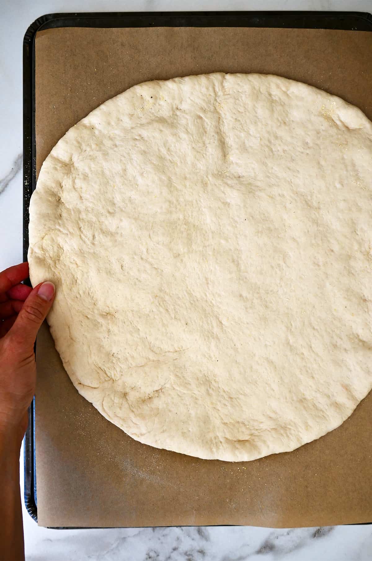 Pizza dough rolled out into a circle on a parchment paper-lined baking sheet.