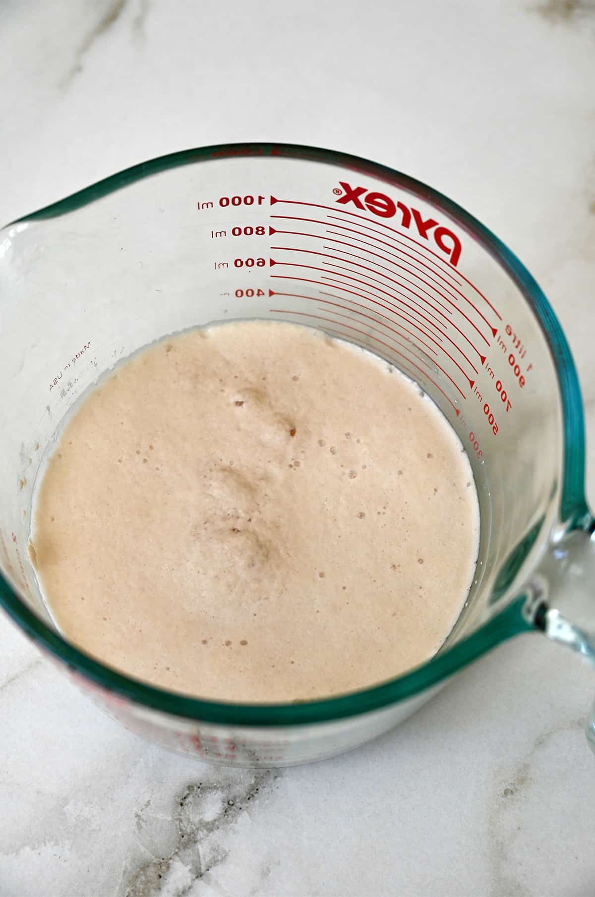 Frothy yeast, sugar and water mixture in a liquid measuring cup. 