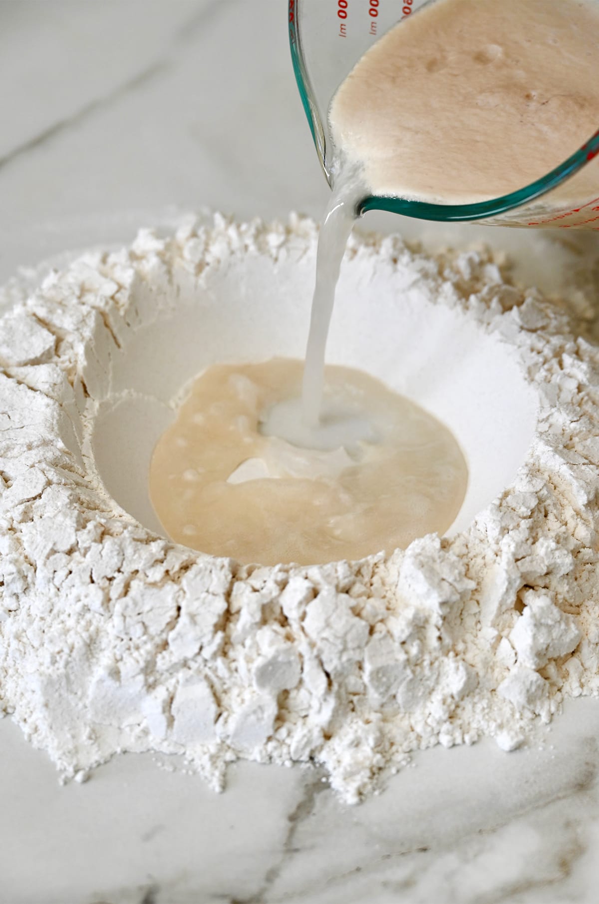 A yeast and water mixture being poured into the well of flour.