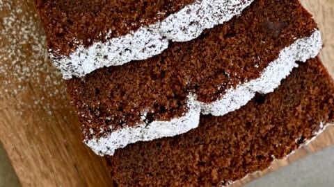 Thick slices of chocolate loaf cake dusted with powdered sugar on a wooden cutting board.