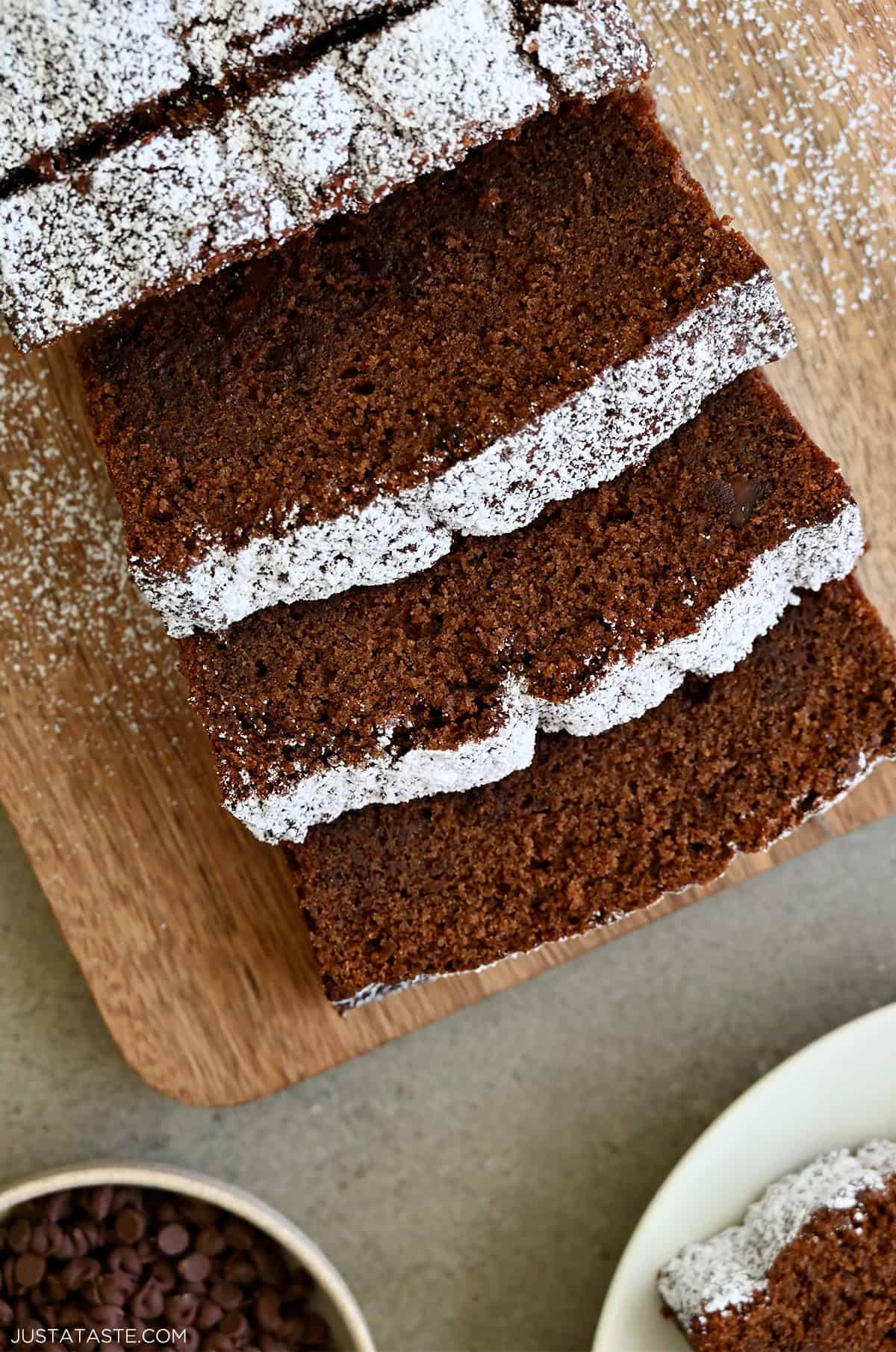 Thick slices of chocolate loaf cake dusted with powdered sugar on a wooden cutting board.