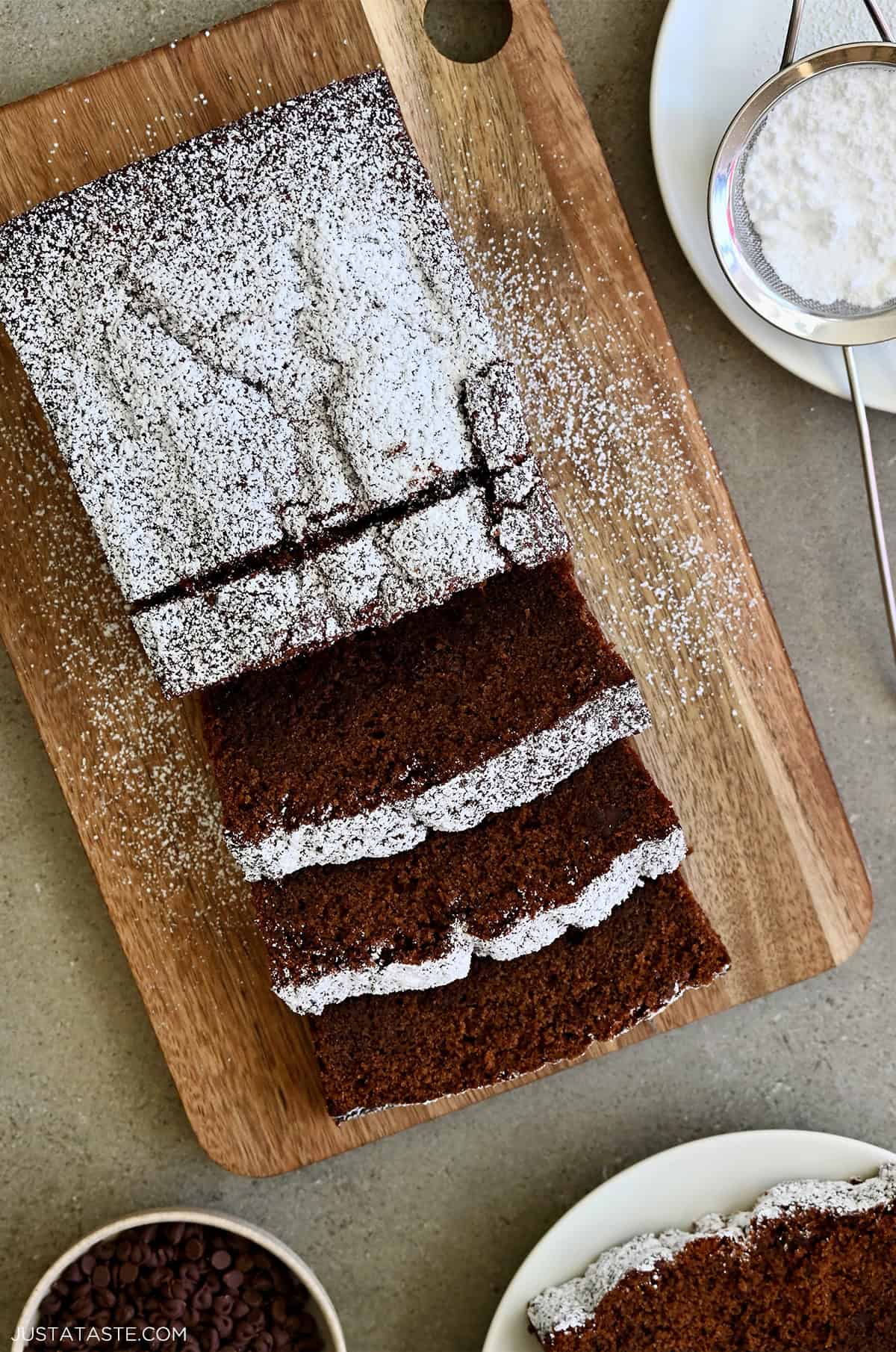 A 9-inch chocolate loaf cake dusted with powdered sugar, with a cracked, rustic top and mini chocolate chips peeking through the crumb.