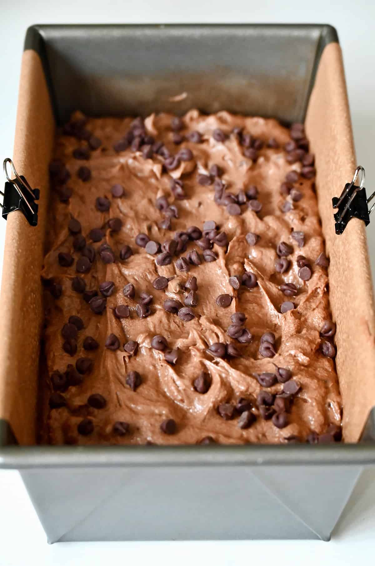 Unbaked chocolate cake topped with mini chocolate chips in a parchment paper-lined 9x5 loaf pan.