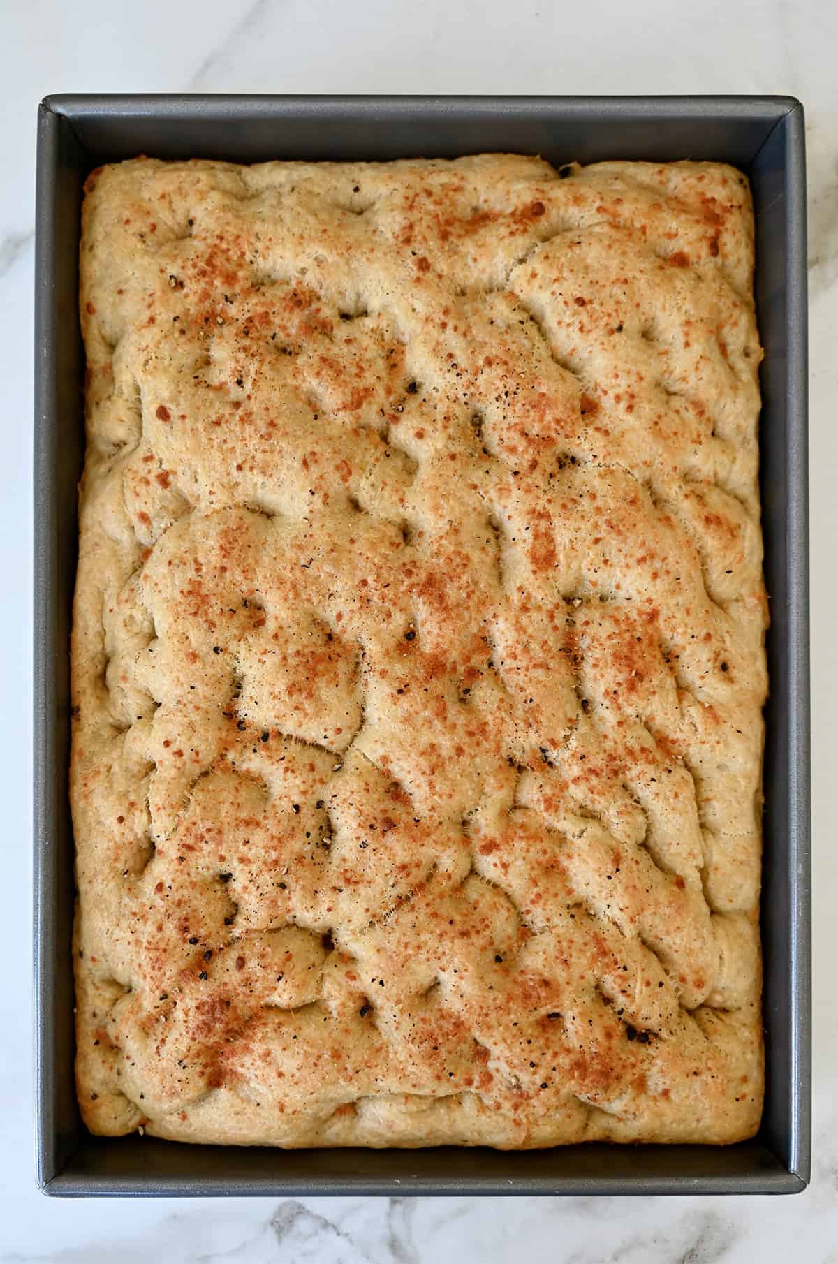 Freshly baked homemade focaccia topped with black pepper and Parmesan cheese.