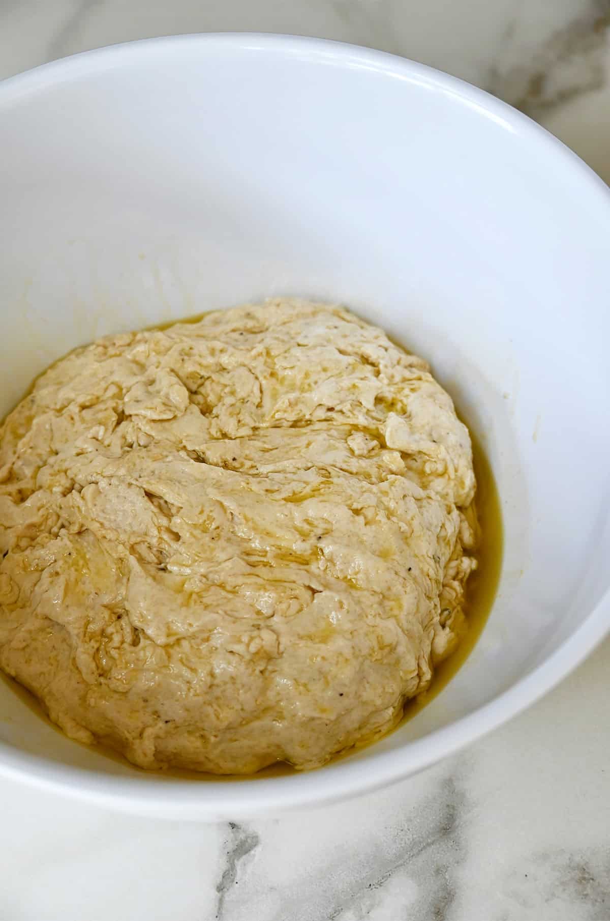 Dough coated in olive oil in a large white bowl.