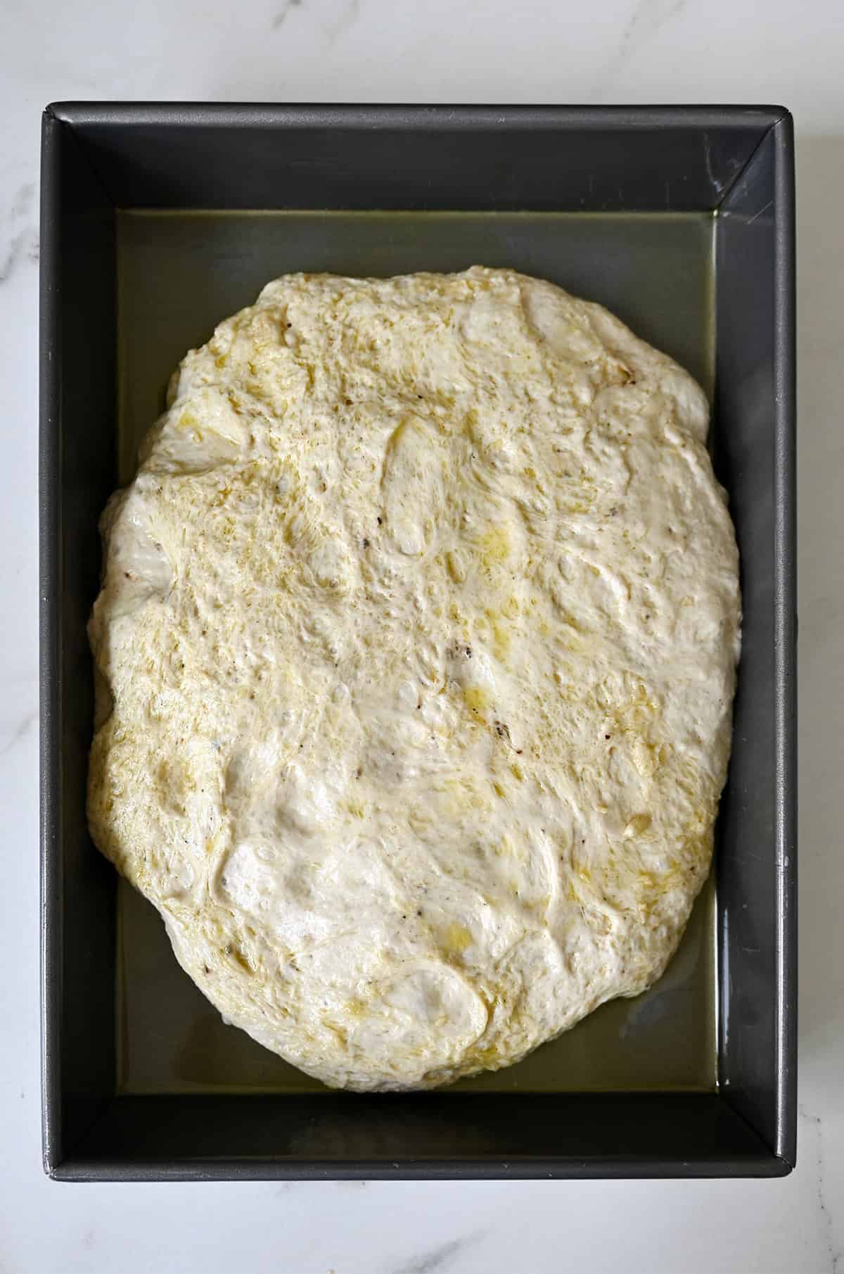 Focaccia dough in a 13x9 metal pan for the second rise.