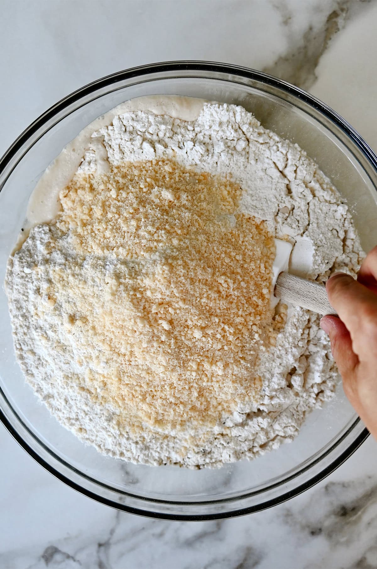 Dry ingredients being incorporated with a water and yeast mixture in a large bowl.
