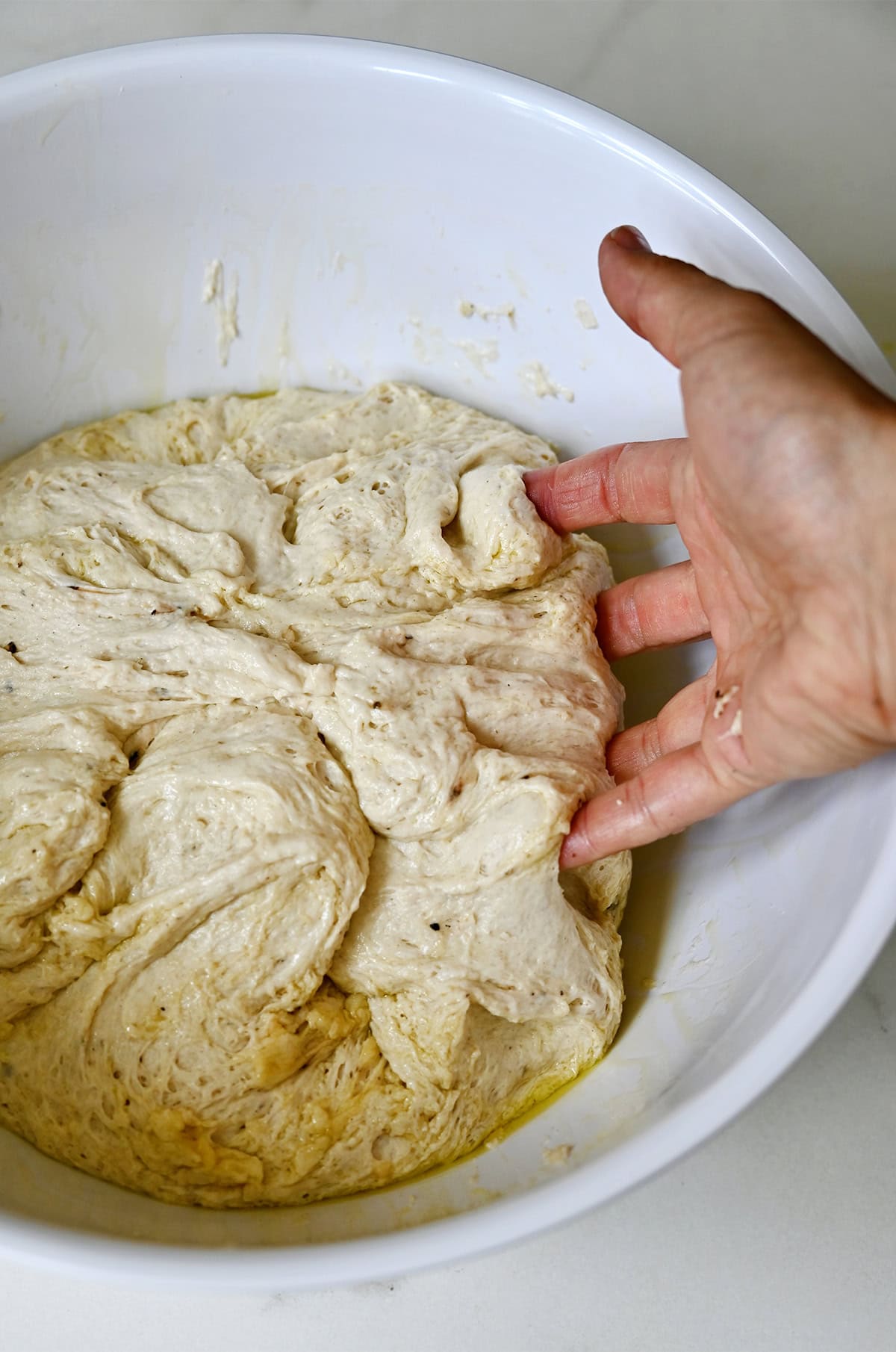 A hand gently folds dough over itself a couple of times in the bowl to deflate it.
