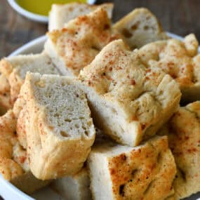 Slices of thick, Parmesan black pepper focaccia bread on a white serving plate.