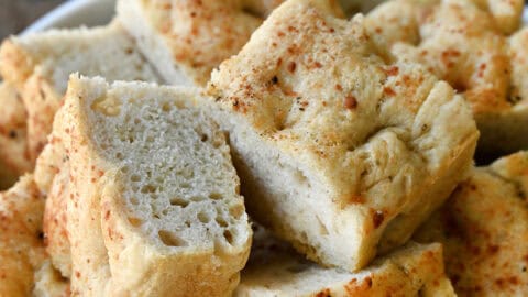 Slices of thick, Parmesan black pepper focaccia bread on a white serving plate.