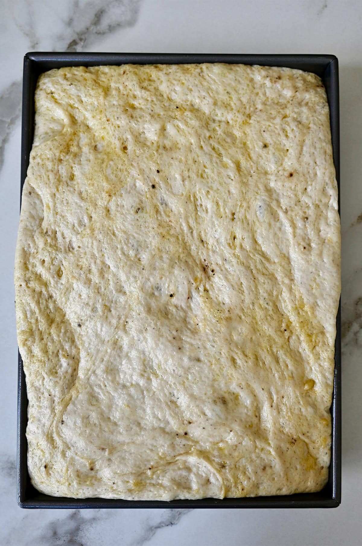 Second proof of focaccia bread dough in a 13x9 metal baking pan.