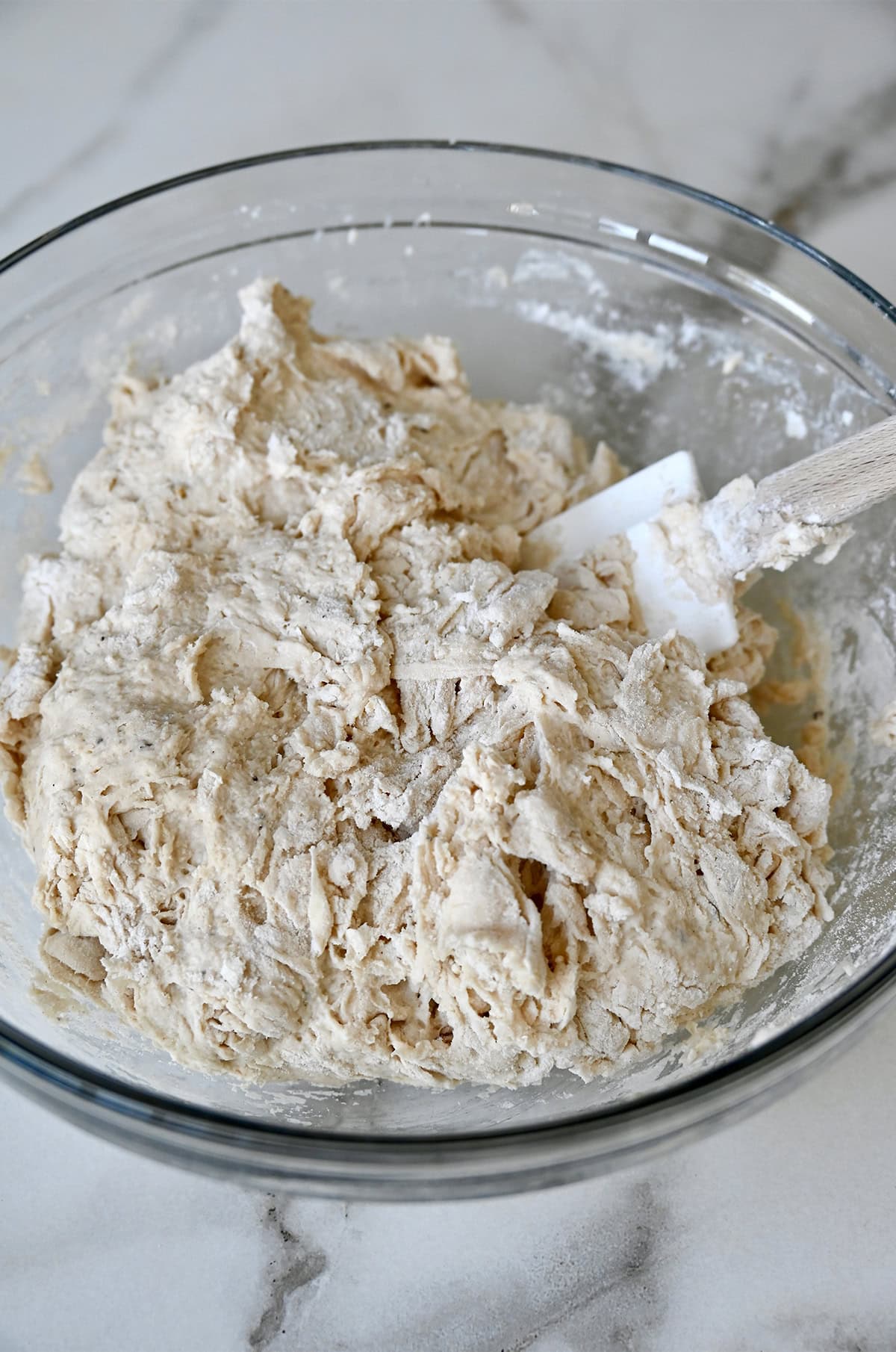 Shaggy focaccia dough in a large glass bowl with a rubber spatula.