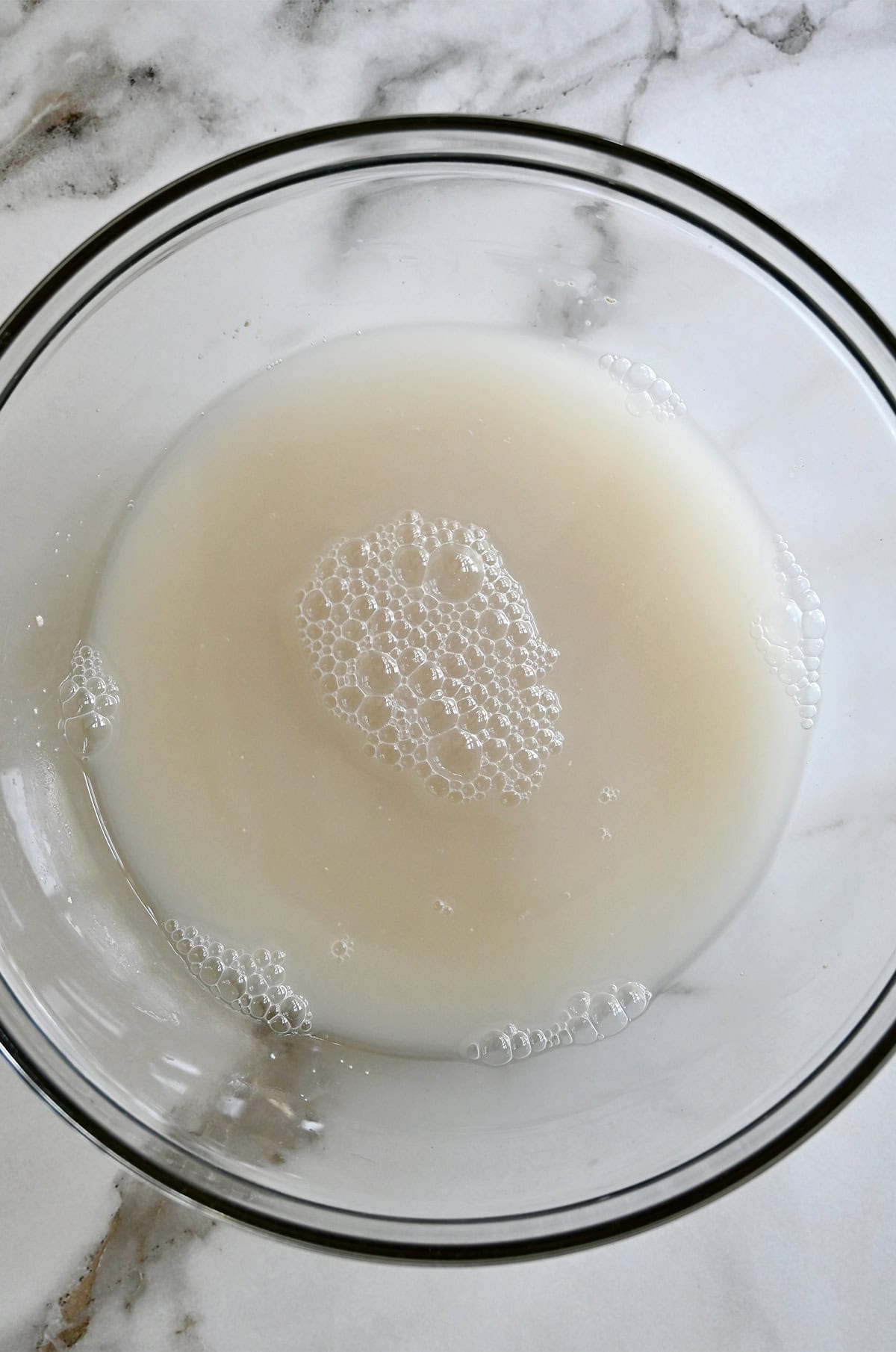 A large glass bowl containing a water and yeast mixture.