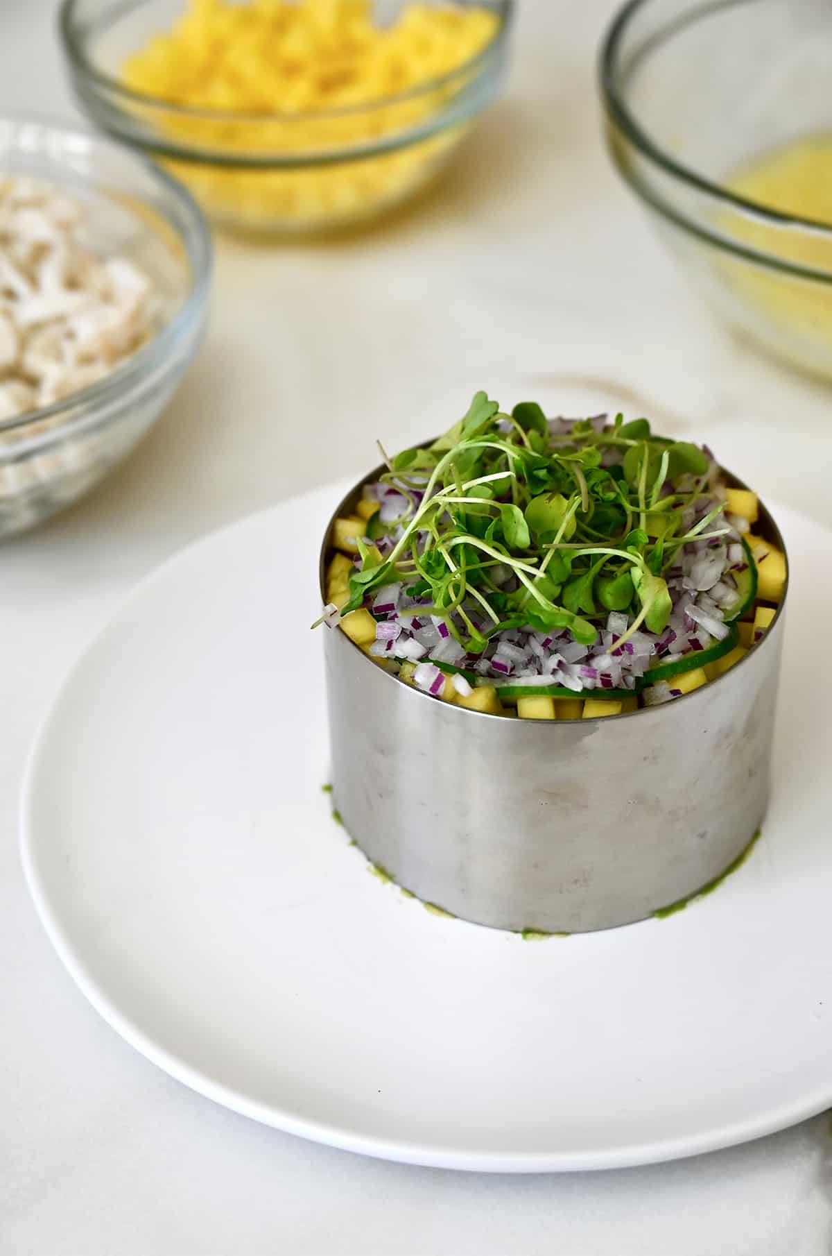 A ring mold on a plate with diced mango, diced red onion and micro greens visible.