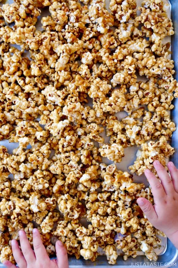 Child's hands on baking sheet of homemade caramel corn