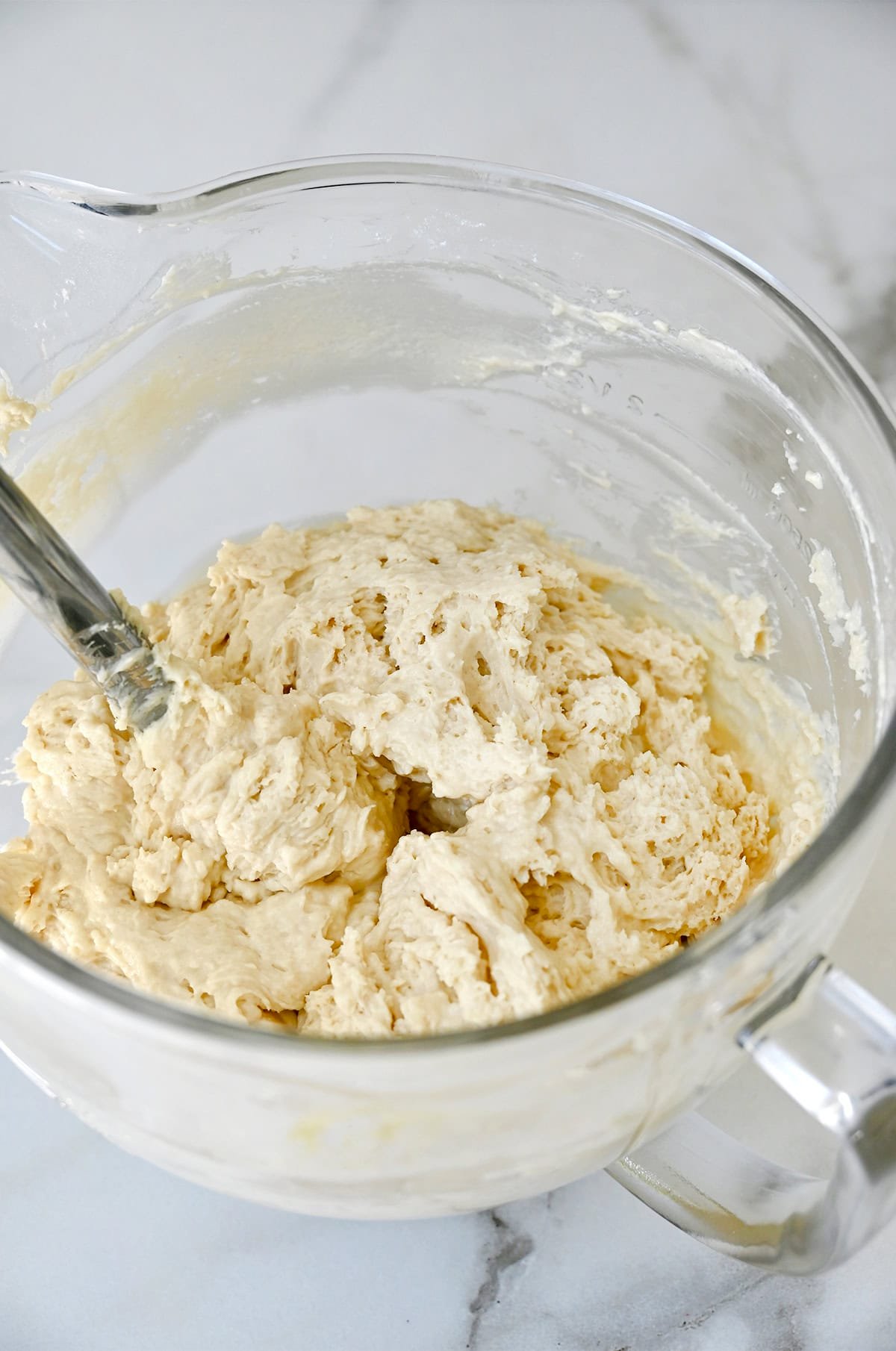 Peach cupcake batter in a glass bowl with a spatula.