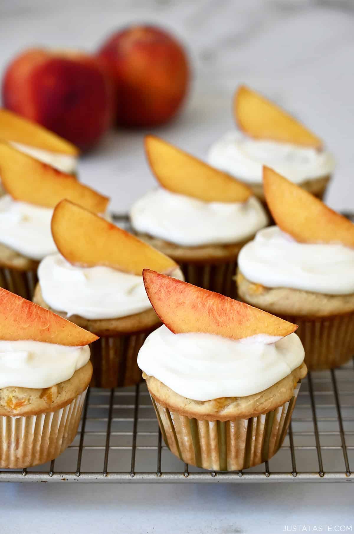 Freshly baked peach cupcakes topped with cream cheese frosting and a peach slice.