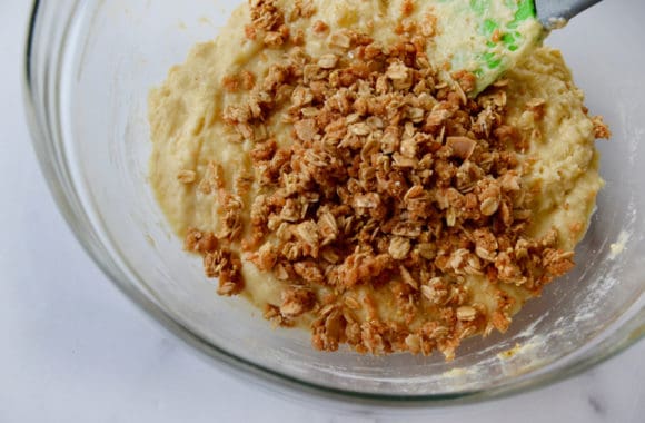 Spatula in glass bowl containing muffin batter with granola 