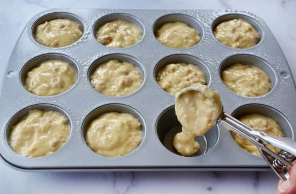 Ice cream scoop filling muffin tin with batter