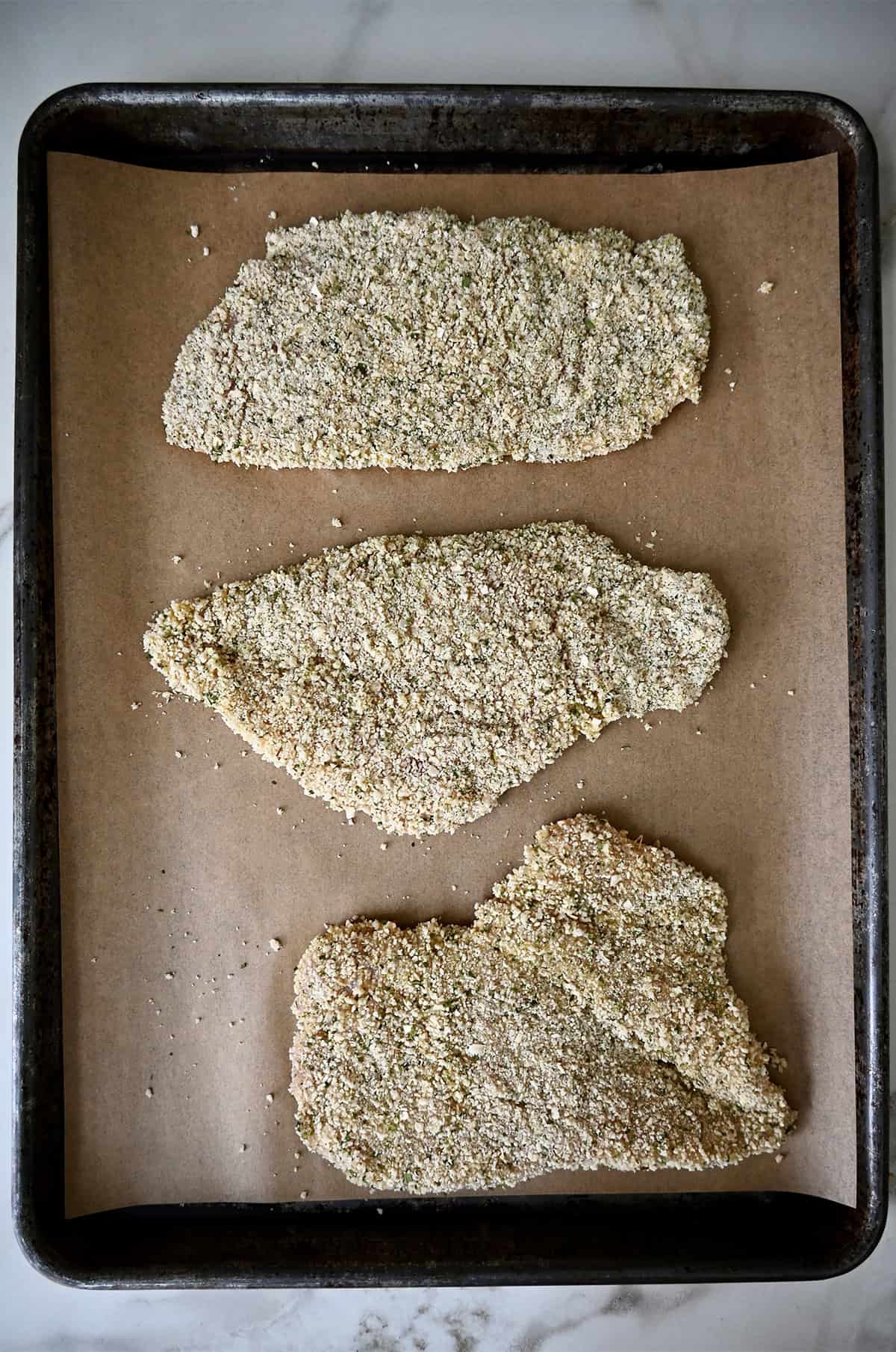 Breaded chicken cutlets on a parchment paper-lined baking sheet.