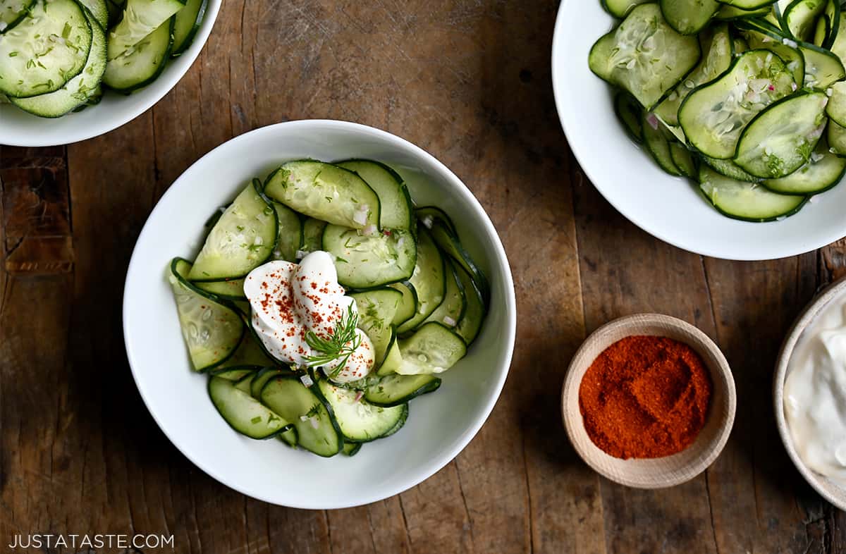 Various bowls containing Hungarian Cucumber Salad topped with Hungarian paprika and a dollop of sour cream.