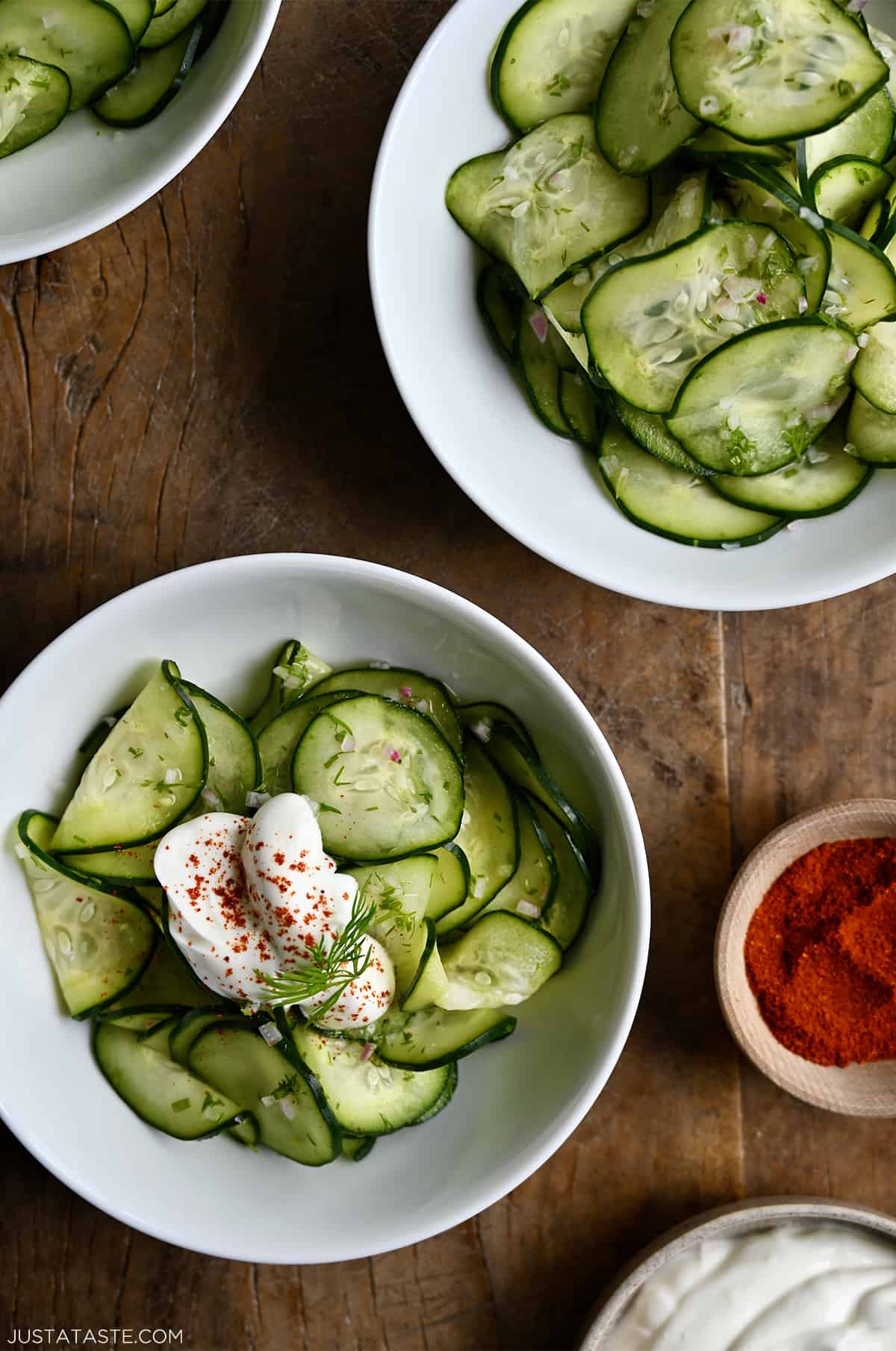 Two white bowls containing Hungarian Cucumber Salad topped with a dollop of sour cream and paprika.