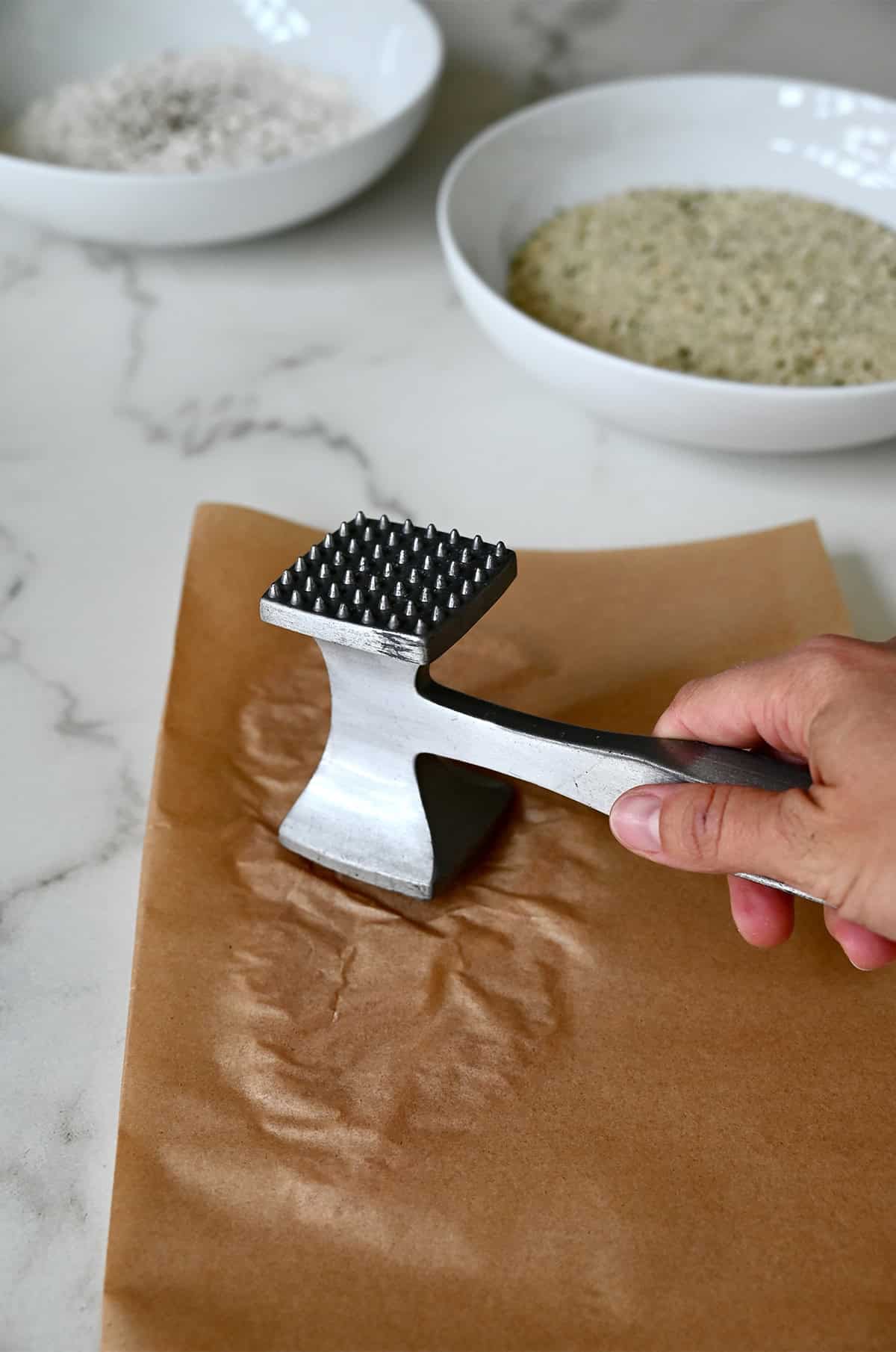 Pounding a chicken breast between two pieces of parchment paper with a meat tenderizer. 