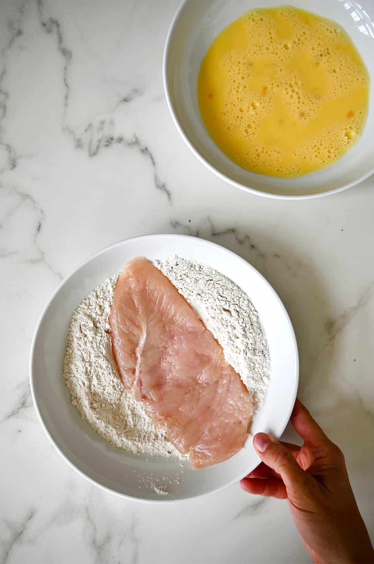 Dredging a chicken cutlet in flour.