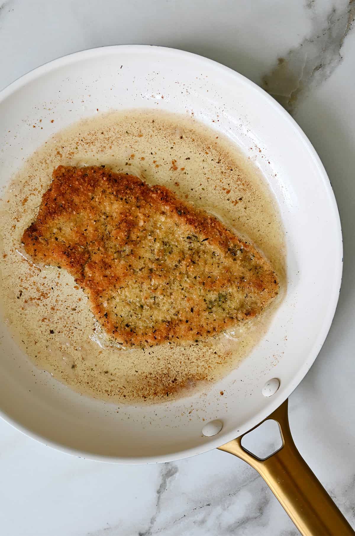 Crispy, golden brown schnitzel in a frying pan with oil.