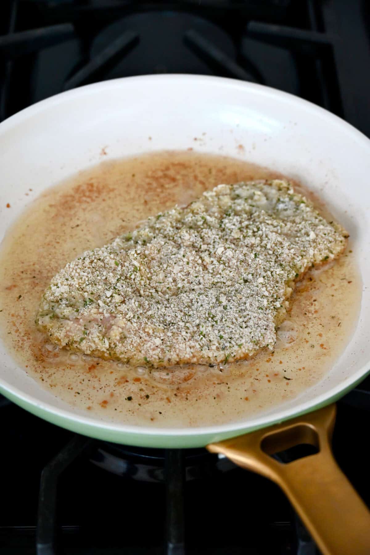 Schnitzel cooking in a skillet on the stovetop.