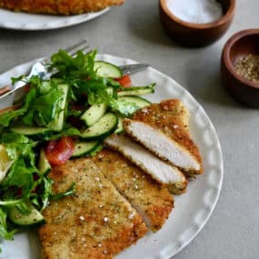 Crispy, golden brown Wiener schnitzel on a white dinner plate with a simple green salad.