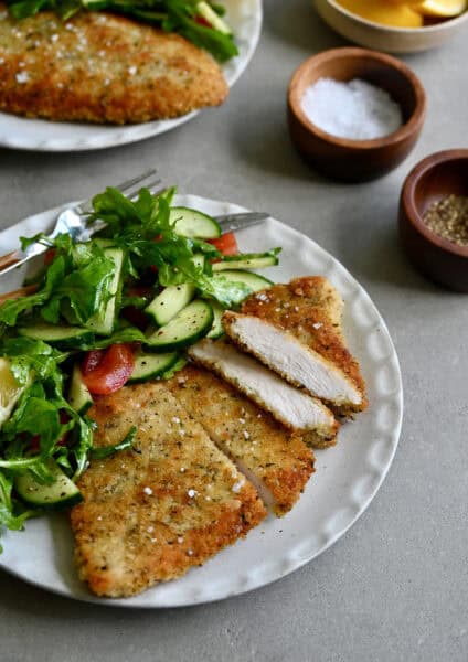 Crispy, golden brown Wiener schnitzel on a white dinner plate with a simple green salad.