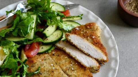 Crispy, golden brown Wiener schnitzel on a white dinner plate with a simple green salad.