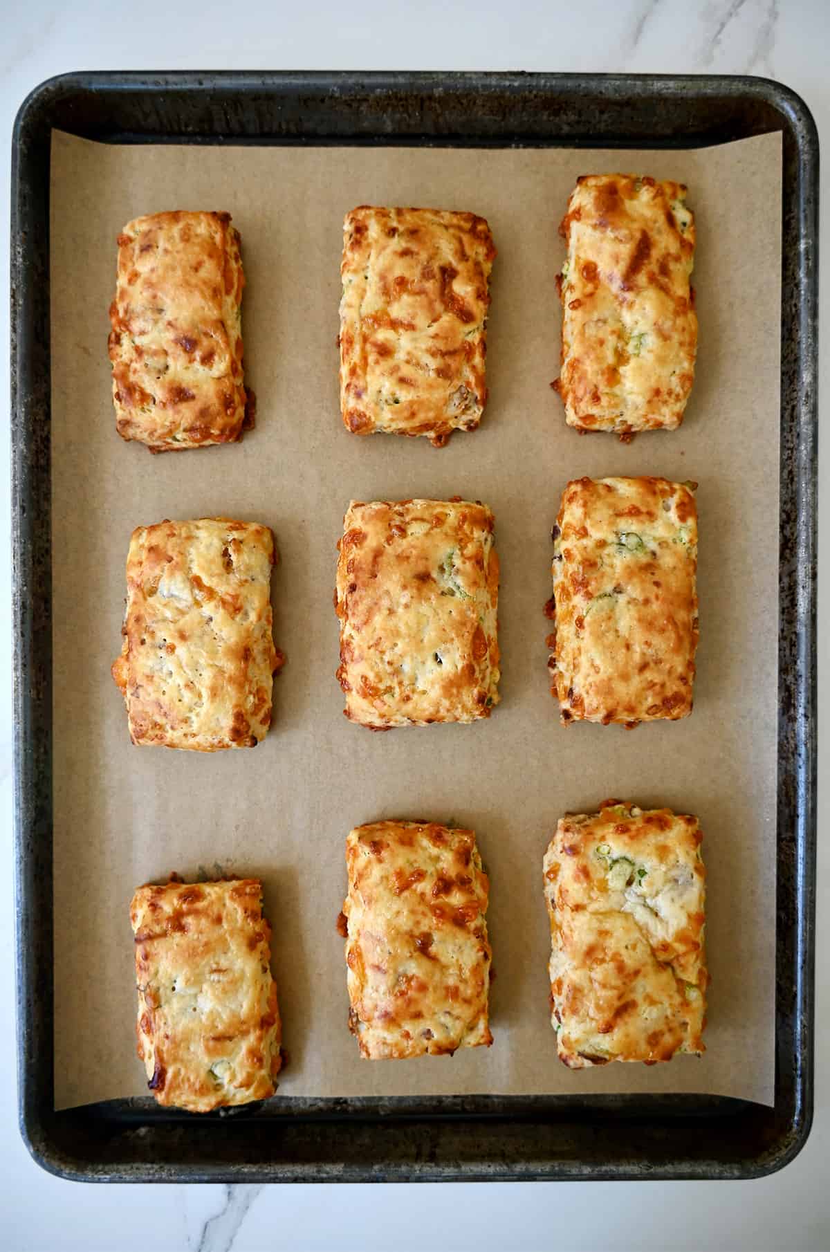 Baked cheesy bacon biscuits on a parchment paper-lined baking sheet.