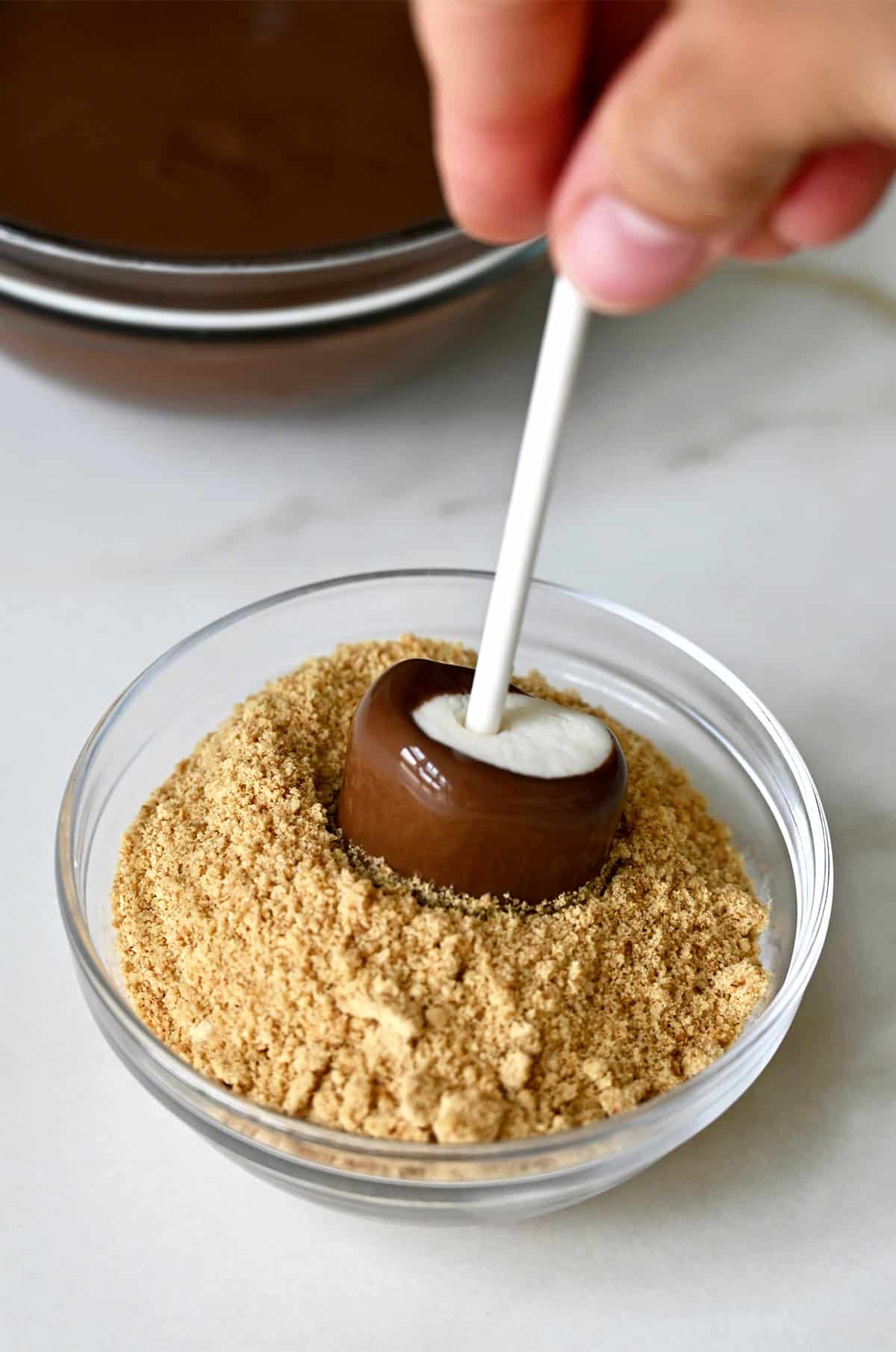 Dipping a chocolate marshmallow pop into crushed graham crackers.