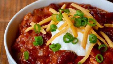 A white bowl containing Turkey Taco Stew topped with sour cream, cheese and scallions