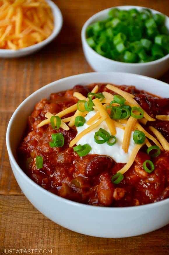 A white bowl containing Turkey Taco Stew topped with sour cream, cheese and scallions