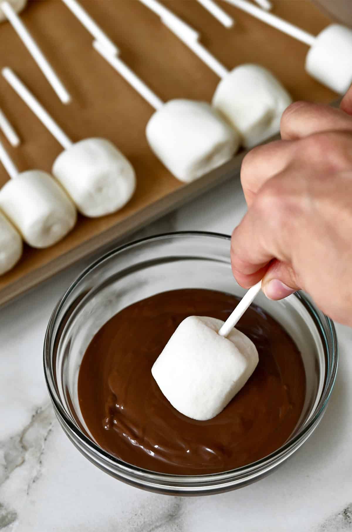 Dipping a marshmallow on a stick into melted chocolate.