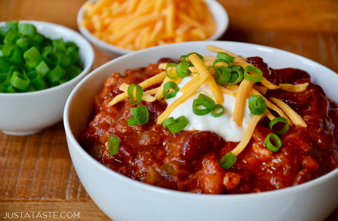 A white bowl of Turkey Taco Stew with small bowls of scallions and cheese