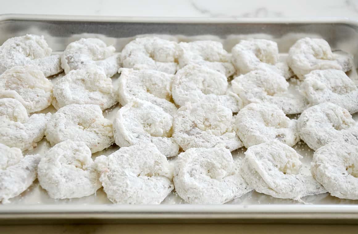 Shrimp covered in cornstarch on a baking sheet.