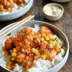 Pineapple shrimp with chopped green peppers tossed in a sweet and spicy sauce atop coconut rice in a bowl with chopsticks.