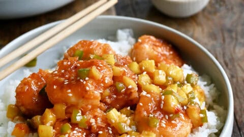 Pineapple shrimp with chopped green peppers tossed in a sweet and spicy sauce atop coconut rice in a bowl with chopsticks.