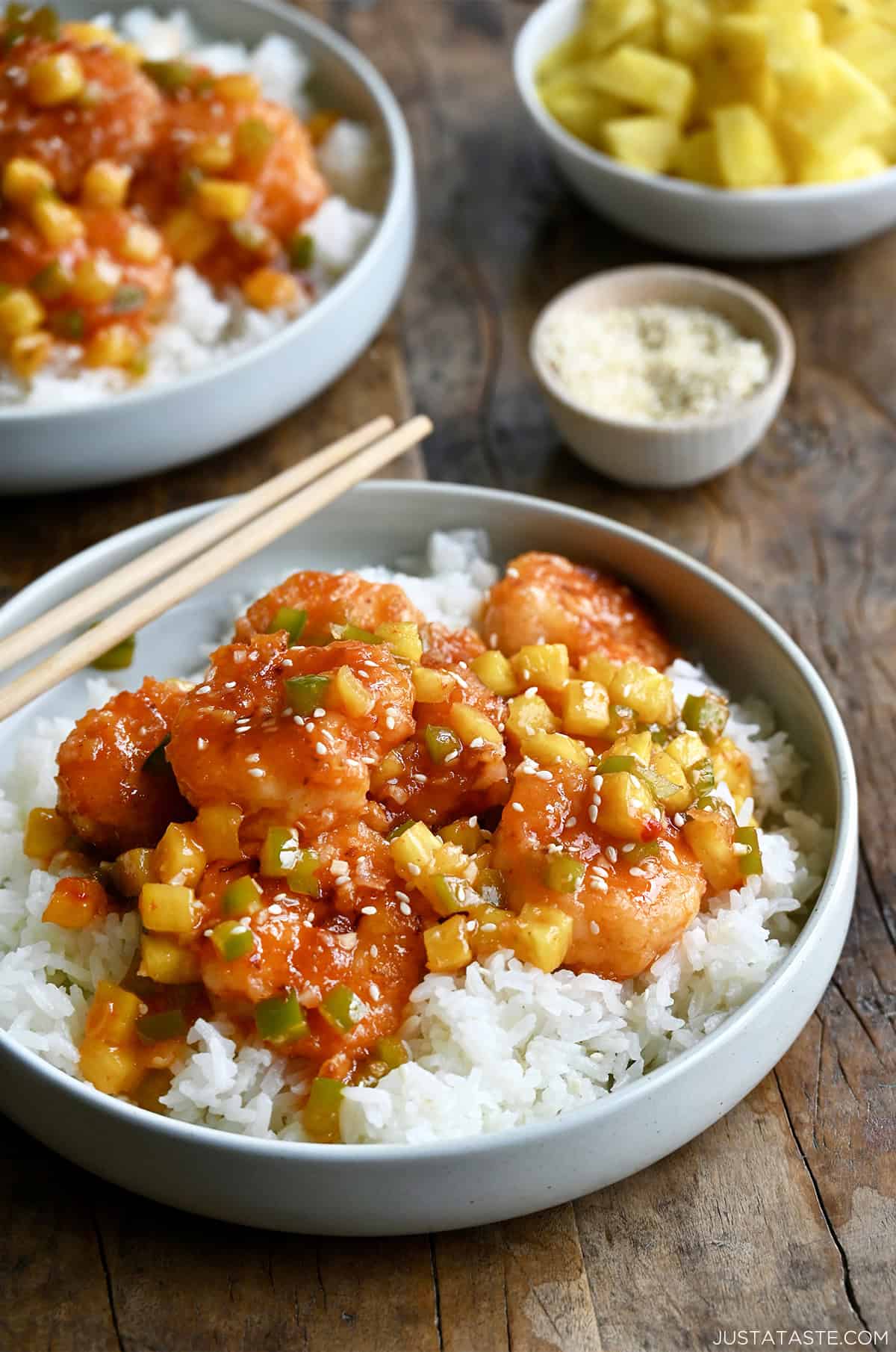 Pineapple shrimp with chopped green peppers tossed in a sweet and spicy sauce atop coconut rice in a bowl with chopsticks.